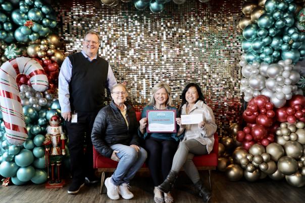 Four adults pose in front of Christmas decorations while holding awards.