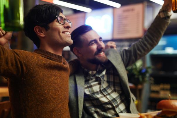 Two friends embracing at a bar and cheering on their favorite team