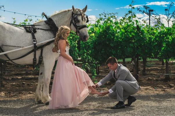 A man kneels to place a shoe on a woman's foot, next to a horse drawn carriage