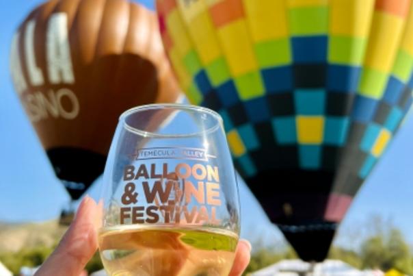 A person holding a glass of wine in front of two hot air balloons