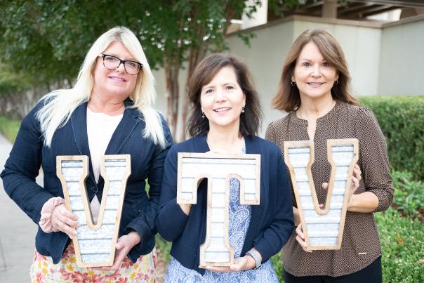 Three women pose with wooden letters that read VTV