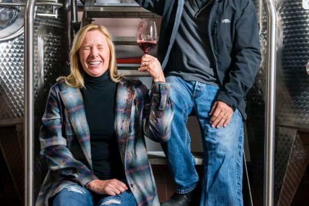 A man and a woman pose while sitting on a metal wine cask
