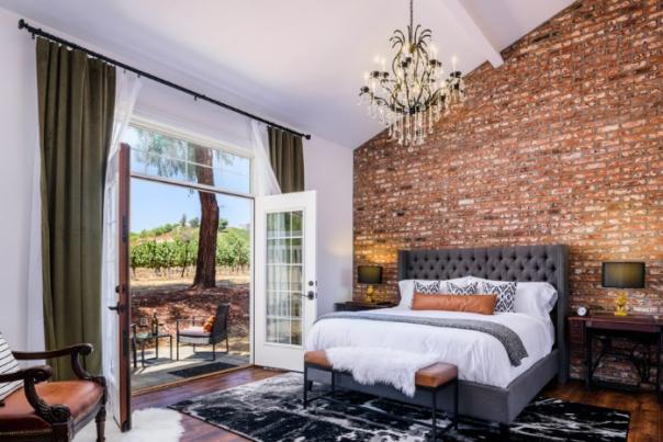 Wide view of a room The Vine House, including a large bed, a balcony, and a red brick wall