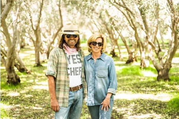 A man and a woman pose under several olive trees