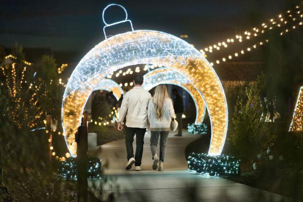 A couple walks through a Chistmas lights decorated path at night