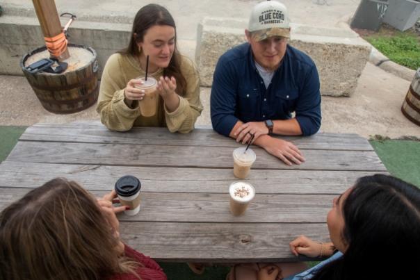 an overhead picture of a group sitting at a picnic table with hot coffees in front of them