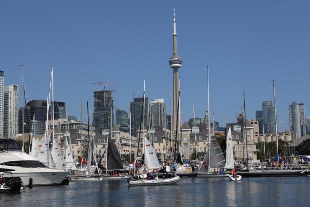 Toronto Harbour with CN Tower in background with several sailboats and people walking by marina