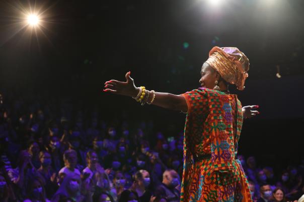 A woman stands in front of a crowd in the Arrell Family Auditorium at CAMH's Suits Me Fine Patient Fashion Show i