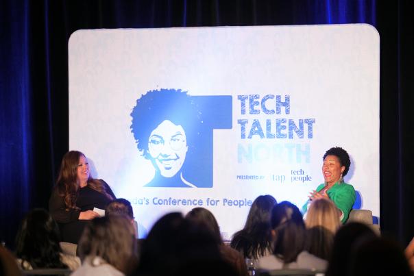 Camille Dundas with a green jacket at the right at Tech Talent North with a panelist on her left in front of a crowd