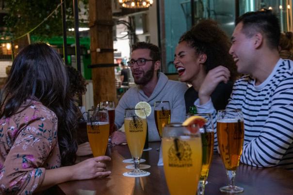 A group of friends laughing and enjoying craft beers at Steam Whistle Brewing's Biergarten, surrounded by a cozy brewery atmosphere with wooden beams and industrial decor