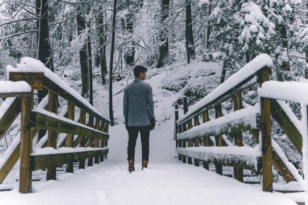 A man walking in the snow over a bridge through a forest