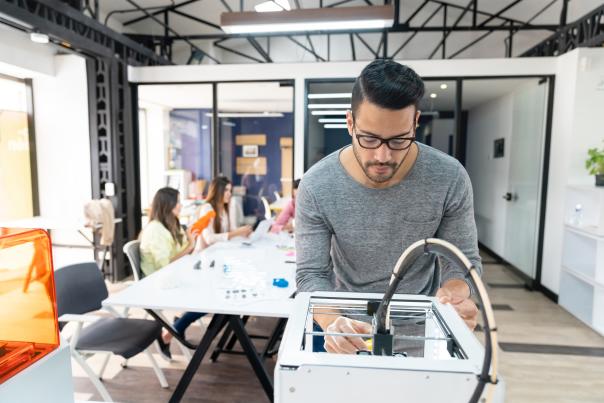 A man looks over 3D printer with team in the background