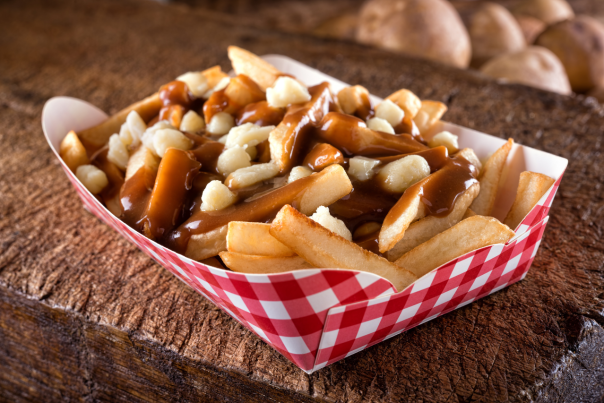 A serving of poutine with french fries, cheese curds, and gravy on a rustic wooden board.