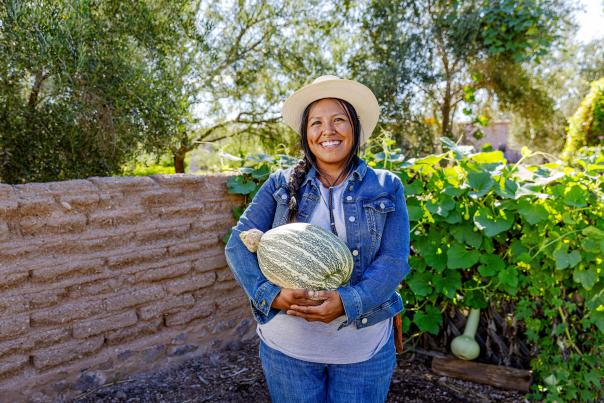 Indigenous Woman at Mission Gardens holding a native fruit that resembles a melon.