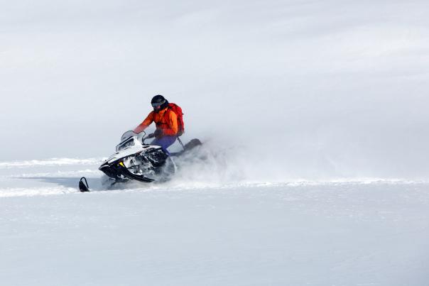Snowmobile rider in red coat through deep powder