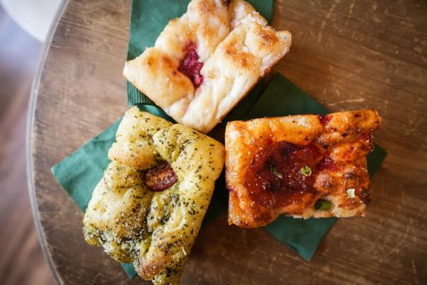 Three specialty focaccia slices, including berry and herb pesto flavors, on a marble counter at F'kosh in Lehi
