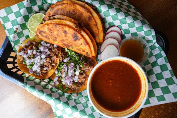 Crispy birria tacos with onion and cilantro beside a cup of red consomme at Red Tacos in Utah County