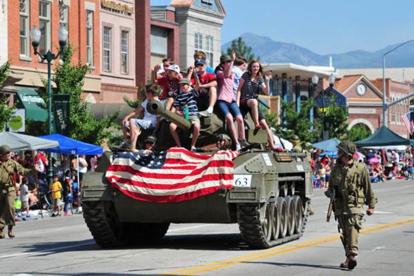 Freedom Festival parade tank going down road with American flag on it and riders on it