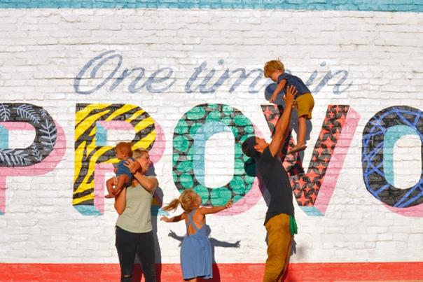 Bucket List Family consisting of 2 adults and 3 kids pose in front of Provo mural that reads "One Time in Provo"