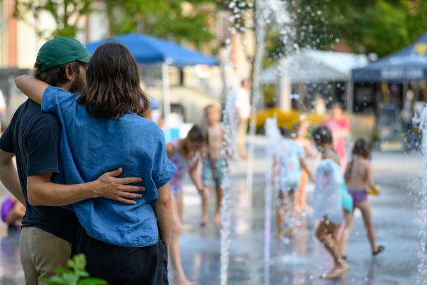 couple embracing as they watch kids splash in a fountain