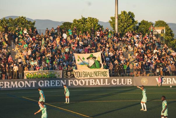 Vermont Green FC players on Virtue Field at sunset with the bleachers in the background.