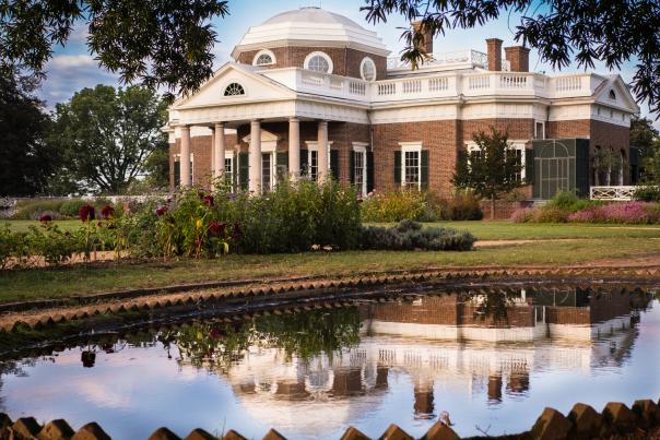 The exterior of Monticello surrounded by folliage, with the reflection of the home showing in a nearby pool