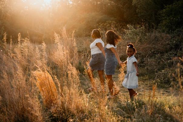 three girls wearing denim and white running through pampas grass at sunset