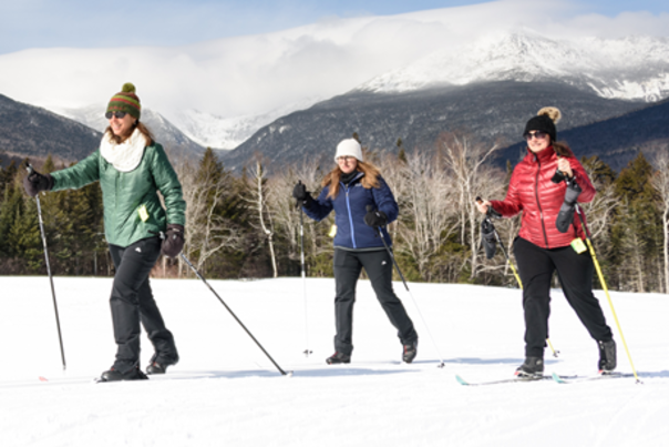 Nordic skiers at Great Glen Trails on a sunny day with a view of Mount Washington in the background