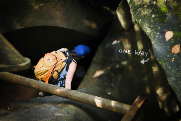 View from above as a woman with an orange backpack enters a cave in New Hampshire.