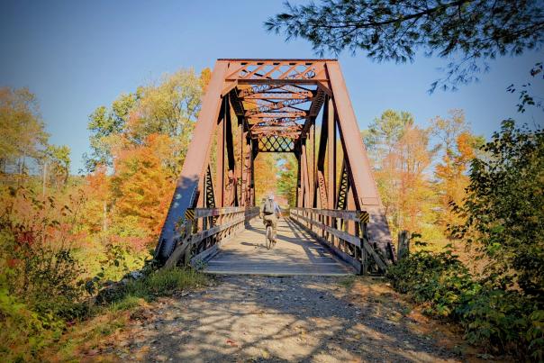Woman biking across trestle bridge with fall foliage in the background