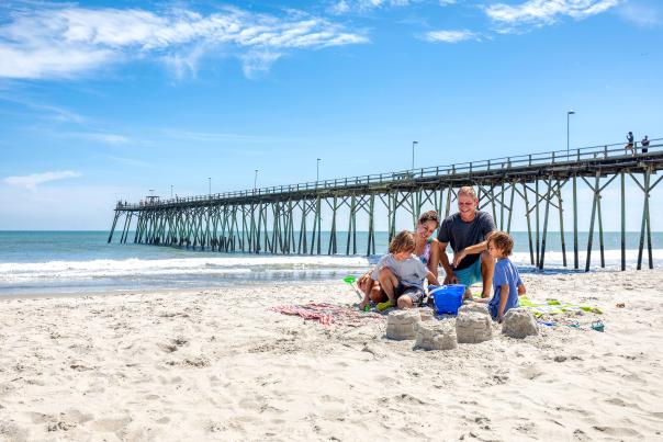 Family hanging out at Kure Beach with Kure Beach Fishing Pier in background