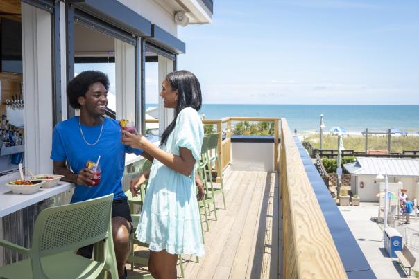 Couple enjoying drinks and fresh acai bowls on the rooftop bar at The Tropical in Carolina Beach.