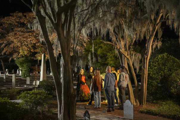 a group of people stand in a cemetery on a ghost tour at night with the guides dressed in old attire