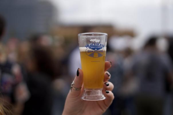 a beer glass filled with a light ale is held up by a lady's hand at the Light House Beer & Wine Festival