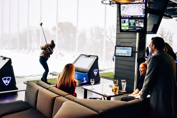 Group at Topgolf with friends enjoying a conversation while a golfer swings at a ball.
