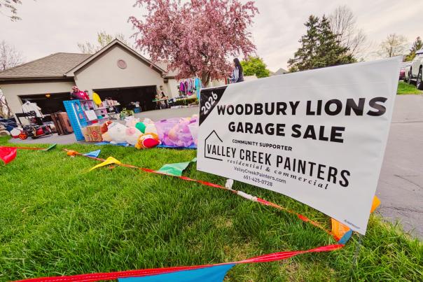 Woodbury Lions Community Garage Sale with official sale sign decorated with pennant banner flags with house and sale items in the background.