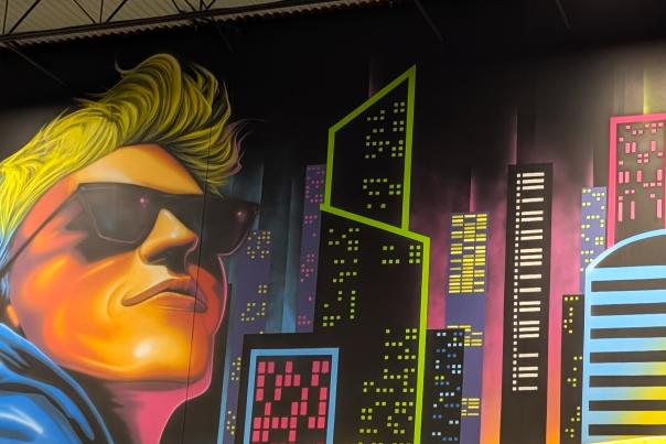 Slick City Action Park showing slide in the foreground with mural painting on the wall of hip adventurer with retro city skyline.