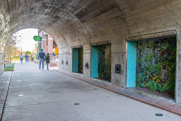 Under the Waterway Avenue Bridge, there is a series of large mosaic panels by Dixie Friend Gay, each depicting a natural landscape or wildlife. The panel nearest the viewer depicts a rabbit peeking out of thick foliage. The tunnel lets out at Goose's Acre.