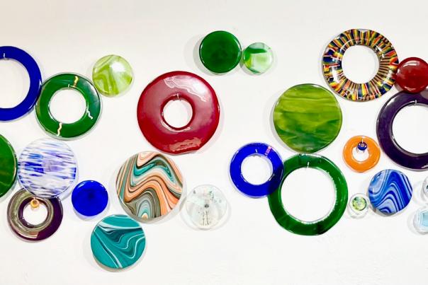 A piece of wall art composed of glass slabs and rings in various sizes, colors, and patterns.