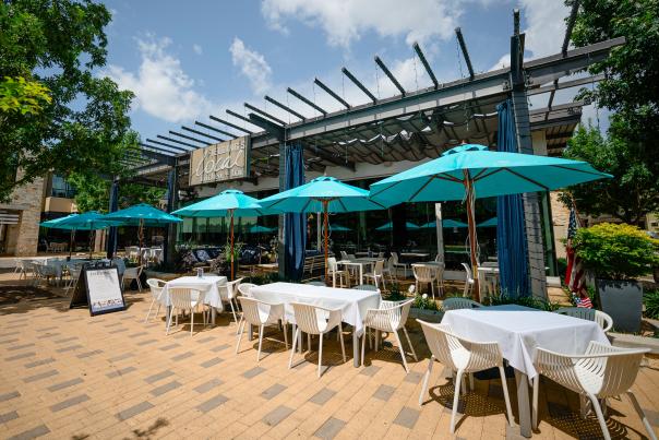 The entrance to Fielding's Local. The building is mostly glass with a shaded patio roof and a sign that reads, "FIELDING'S local kitchen + bar" in various font types. Patio tables are each shaded by large turquoise umbrellas.