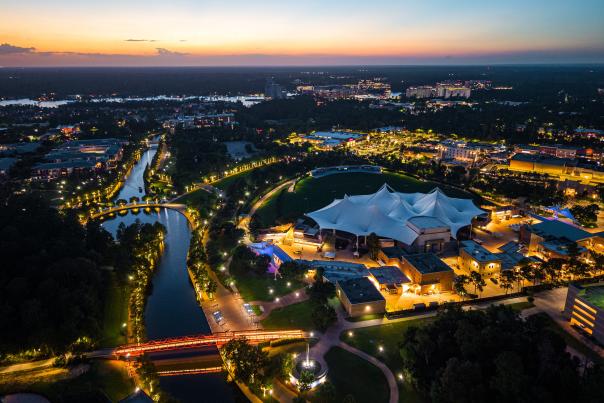 An aerial drone view of The Pavilion during late sunset. The camera hovers over the new apartments along The Waterway, facing The Pavilion, Riva Row, Market Street, and more, all glowing gold as the sun goes down.