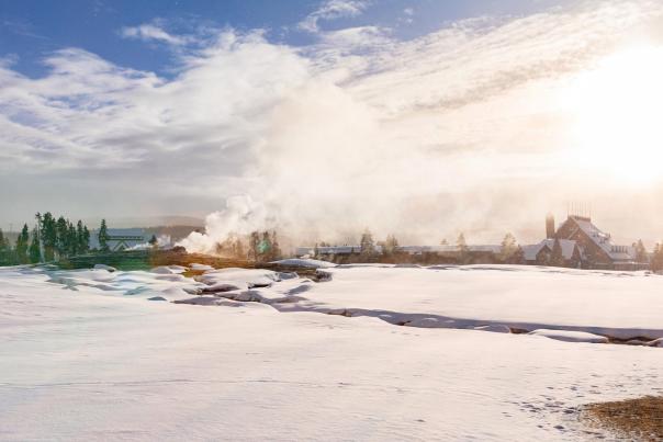 Old Faithful geyser and Old Faithful Inn in Yellowstone's Upper Geyser Basin during the winter, with snow on the ground.