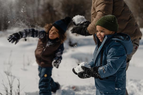 Two children play in fresh snow during a winter outing near Jackson, Wyoming. Dressed in warm winter clothing, the children toss and hold snow while enjoying the snowy landscape, highlighting family-friendly winter recreation in Teton County.