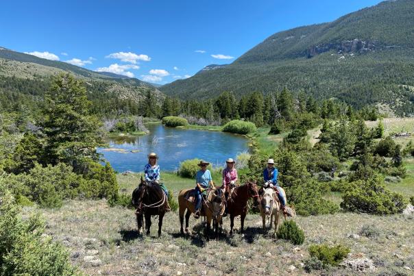Authentic ranch experience: Four friends enjoying a guided horseback ride on a high-country trail at The Hideout Lodge, overlooking a scenic lake