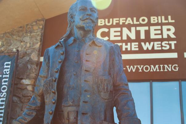 Bronze statue of Buffalo Bill Cody standing outside the Buffalo Bill Center of the West in Cody, Wyoming, with the museum’s name visible in the background.