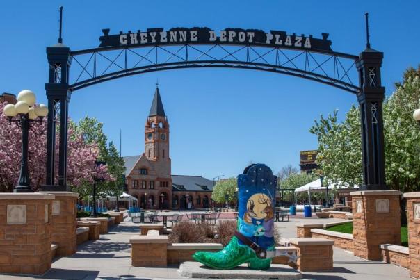 A colorful scene at Cheyenne Depot Plaza, where a painted cowboy boot stands in the middle of the courtyard as vibrant trees bloom in the background before big clock tower. 