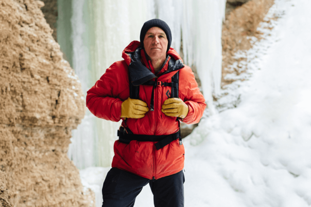 Aaron Mulkey in a red jacket and black hat standing in front of a frozen waterfall