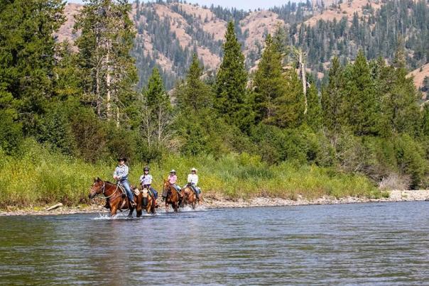 Horseback riders on river side at a dude ranch in Wyoming during the summertime.