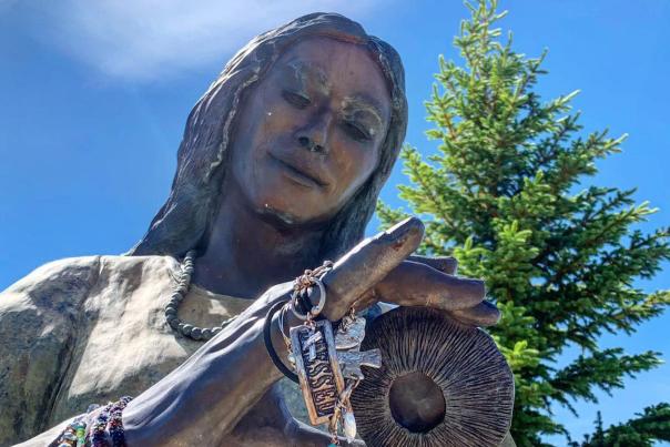 Statue of Sacajawea against blue sky and green tree in background