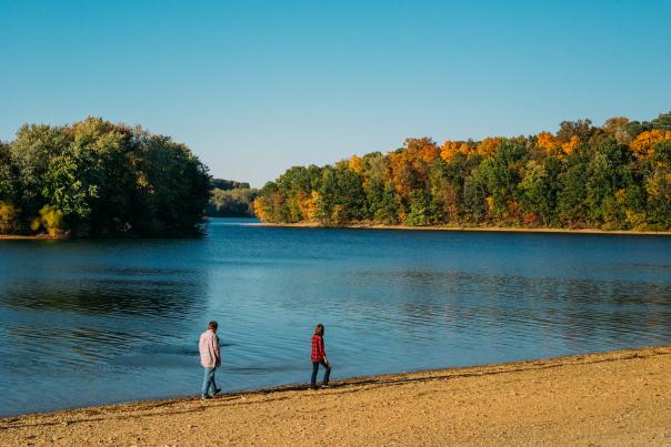 Image of two people strolling along the lake shore in fall under a bright blue sky